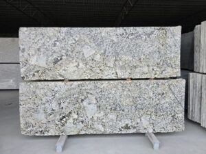 Front view of Alaska White polished granite slabs showcasing their natural white, grey, and black mineral veining pattern. Large-format premium stone slabs displayed in a warehouse environment, ideal for countertops, flooring, and luxury interior applications