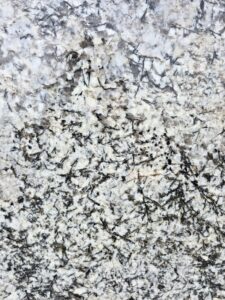 Close-up shot of Alaska White polished granite texture featuring detailed white feldspar crystals, bold grey veining, and natural pattern variations. High-resolution granite surface ideal for showcasing stone quality for interior and architectural use.