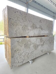 Imperial Alaska White polished granite slabs stacked in a warehouse, showcasing their light cream and white background with natural grey and black mineral patterns. Premium quality granite ideal for countertops, flooring, and luxury home interiors.”