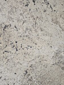 “Close-up texture of Imperial Alaska White polished granite showing intricate white feldspar crystals, grey swirls, and dark mineral specks. High-resolution surface detail for showcasing quality of premium natural stone for interior architecture.”