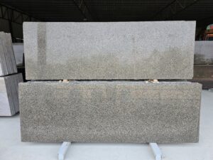 Front view of Apple Green Leather Finish Granite slabs featuring a textured matte leather surface with a mix of green, grey, and brown mineral grains. Premium natural stone displayed in a warehouse, ideal for countertops, flooring, and interior applications.